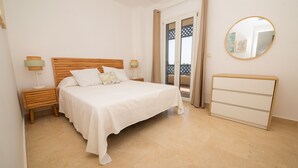 Quarto com cama, mesas de cabeceira, cômoda e porta que dá para uma varanda.