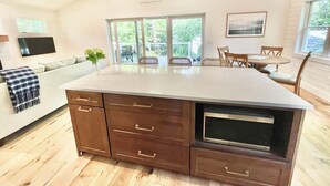 Cocina amplia con una isla grande, gabinetes de madera y microondas integrado. Cuenta con una zona de comedor con mesa y sillas, y un ventanal que proporciona luz natural.