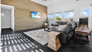 A modern living room with a wooden accent wall, a large sofa, a coffee table, and a fireplace. - Serenity: Private Pool + Golf + Sand Dunes (Hurricane)