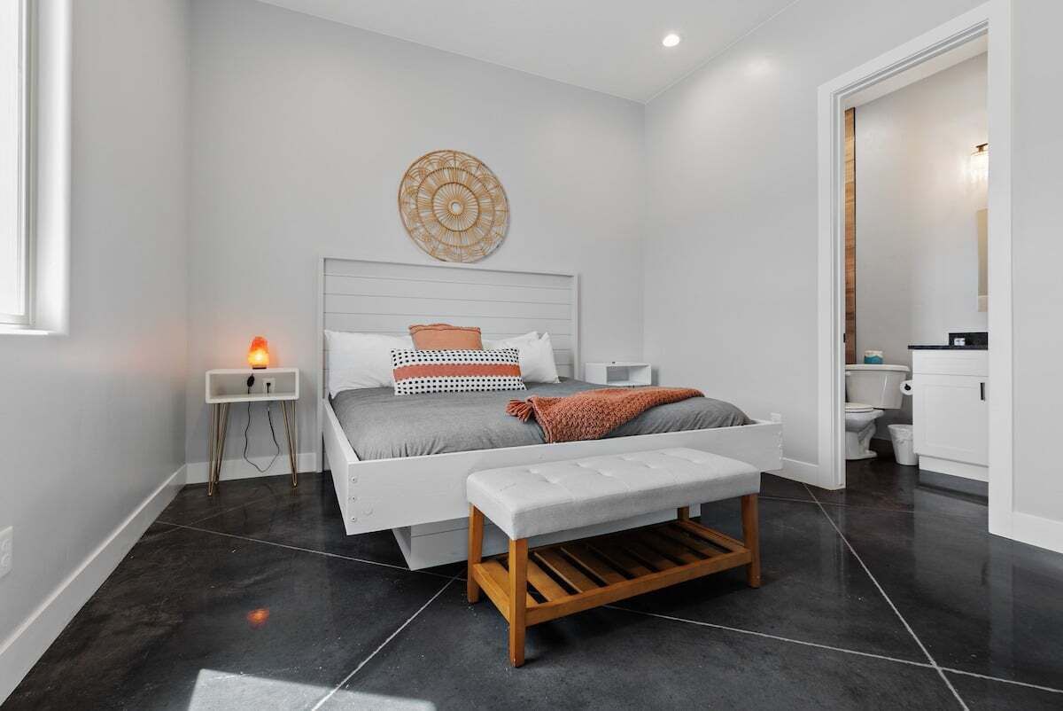 Une chambre moderne avec un grand lit, des tables de chevet, un banc et un élément décoratif fixé au mur.