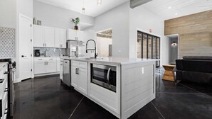 A modern kitchen with white cabinetry, a central island, and a black tiled floor. - Serenity: Private Pool + Golf + Sand Dunes (Hurricane)
