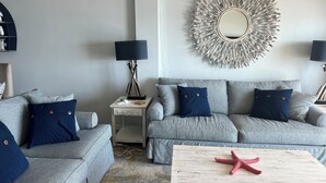 A living room with a grey sofa set, a white coffee table, and a decorative mirror on the wall. - Ocean Front Condo (New Smyrna Beach)
