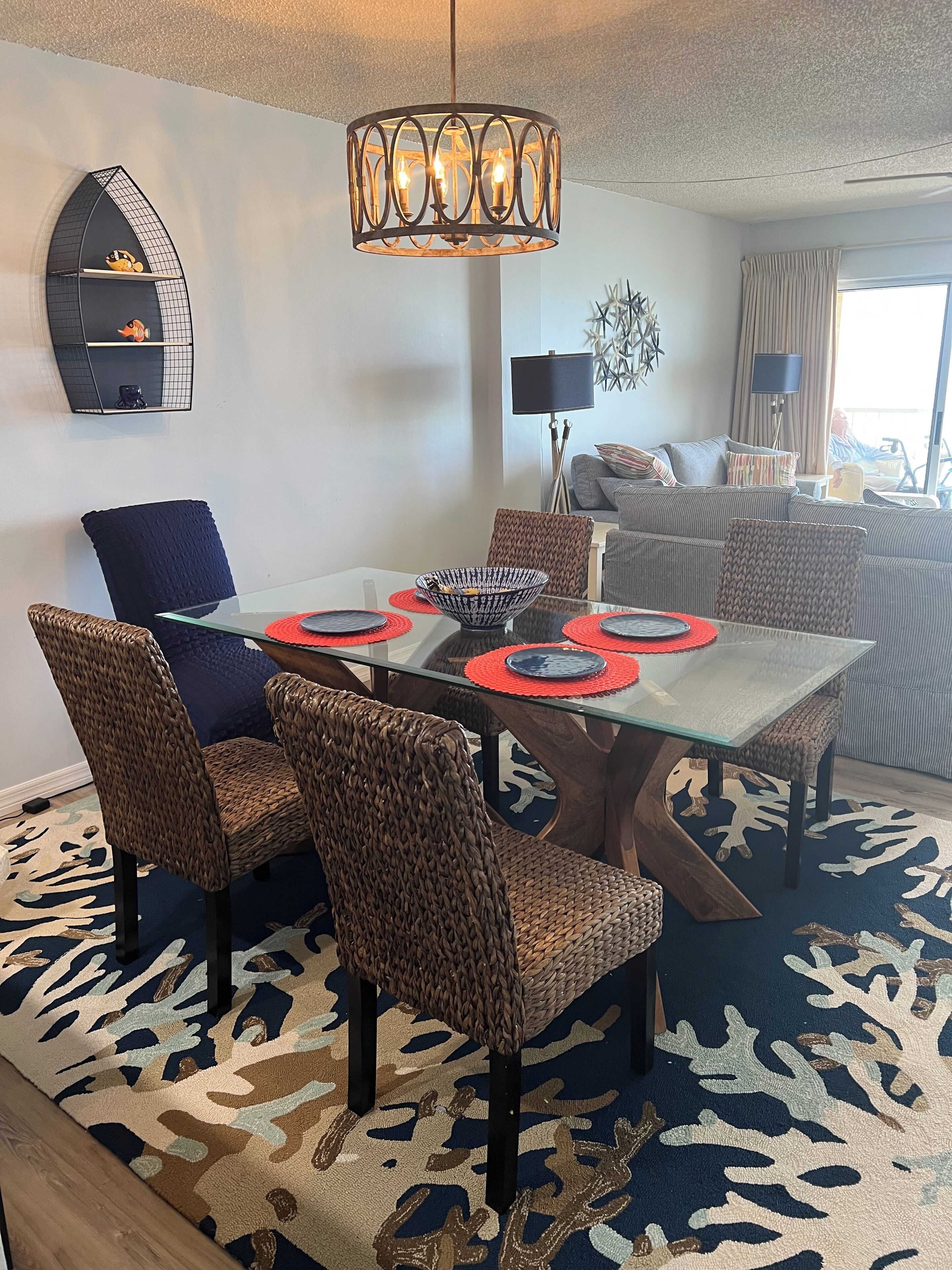 A dining area with a glass table, wicker chairs, and a patterned rug.