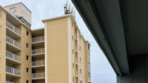 A high-rise building with multiple balconies and a swimming pool area with lounge chairs. - Ocean Front Condo (New Smyrna Beach)