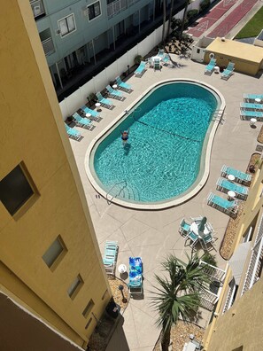 A swimming pool surrounded by lounge chairs and sunbeds, with a building in the background.