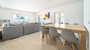 A modern living room with a large sofa, a wooden dining table, and grey chairs. - Villa Ribeiro by HelloVacations (Albufeira)