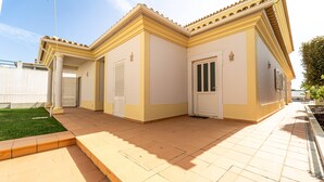 A two-story building with a yellow facade, a tiled patio, and a small lawn area. - Villa Ribeiro by HelloVacations (Albufeira)