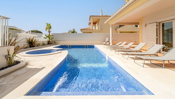 A swimming pool with lounge chairs and a hot tub, surrounded by a white fence and plants. - Villa Ribeiro by HelloVacations (Albufeira)