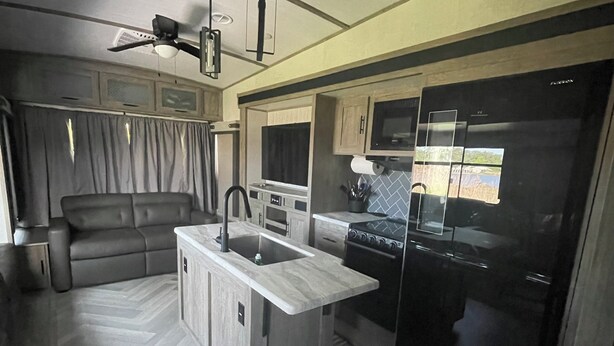A compact RV kitchen with a central island, a stove, and a refrigerator.
