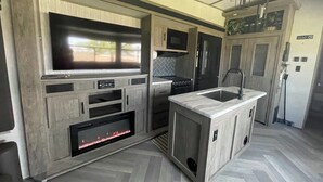 A modern kitchen with a flat-screen TV, built-in oven, microwave, and a small sink.