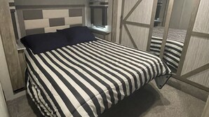 A bedroom with a bed, a nightstand, a mirror, and a door.