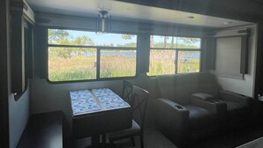 A compact interior with a table and two chairs, large windows offering a view of a natural landscape.
