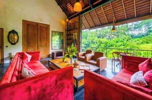 Relax in a serene space with a sofa, coffee table, and chairs, surrounded by lush greenery views.