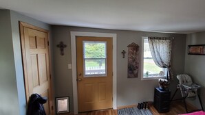 Una habitación con puerta de madera, ventana con vistas al exterior, una silla y una mesita con objetos encima.