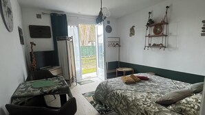 Ein Zimmer mit Bett, Schreibtisch, Stuhl, kleinem Tisch, einer Hängeleuchte und Blick durch eine Tür.