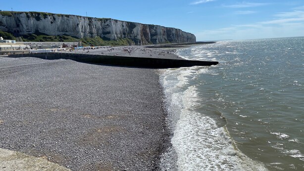 Ein Kiesstrand mit einer Klippe im Hintergrund.