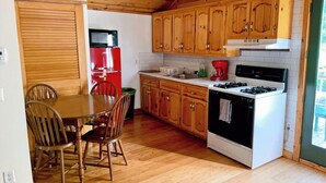 A compact kitchen with wooden cabinets, a red refrigerator, a stove, and a dining area with chairs.