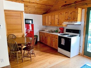 A compact kitchen with wooden cabinets, a red refrigerator, a stove, and a dining area with chairs.