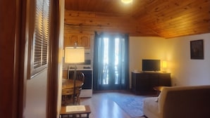 A wooden-paneled room with a dining area, a sofa, a TV, and a lamp.