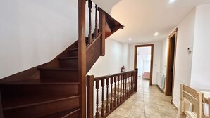 Una escalera de madera con barandilla que lleva a un piso superior. Un extintor está montado en la pared cerca de la escalera.