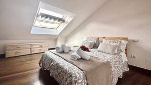 Un dormitorio con tragaluz, una cama con colcha estampada, una mesita de noche y un aparador de madera.