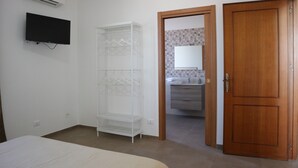 Une chambre à coucher comprenant un lit, un téléviseur fixé au mur, une armoire et une porte donnant sur une salle de bain.
