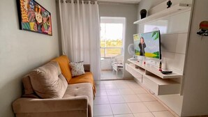 Een moderne woonkamer met een beige bank, een flatscreen televisie, een plafondlamp en een raam met gordijnen.