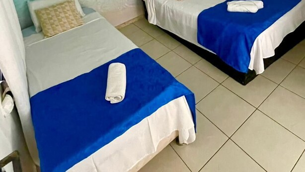 Een kamer met twee bedden, elk met een blauw-witte dekbedovertrek, en een plafondventilator.