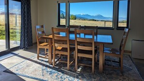 Een eetgedeelte met een tafel en stoelen, grote ramen met uitzicht op een berg, en een plafondlamp.