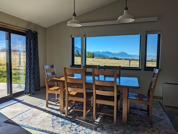 A dining area with a table and chairs, large windows with a mountain view, and a ceiling light fixture.
