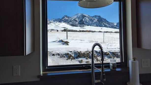 Een badkamer met een groot raam, met uitzicht op besneeuwde bergen.