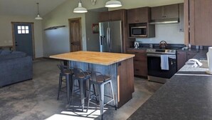 Een ruime keuken met een centraal eiland, barstoelen, een koelkast, magnetron, fornuis en een plafondventilator.