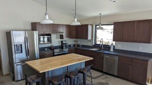 Een moderne keuken met donkerhouten kastjes, roestvrijstalen apparatuur, een centraal eiland met barkrukken en hanglampen.