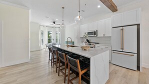 A modern kitchen with white cabinetry, a large island with bar stools, stainless steel appliances, and a wooden ceiling beam. - Gulf Place Spires #7B by Southern Vacation Rentals (Santa Rosa Beach)
