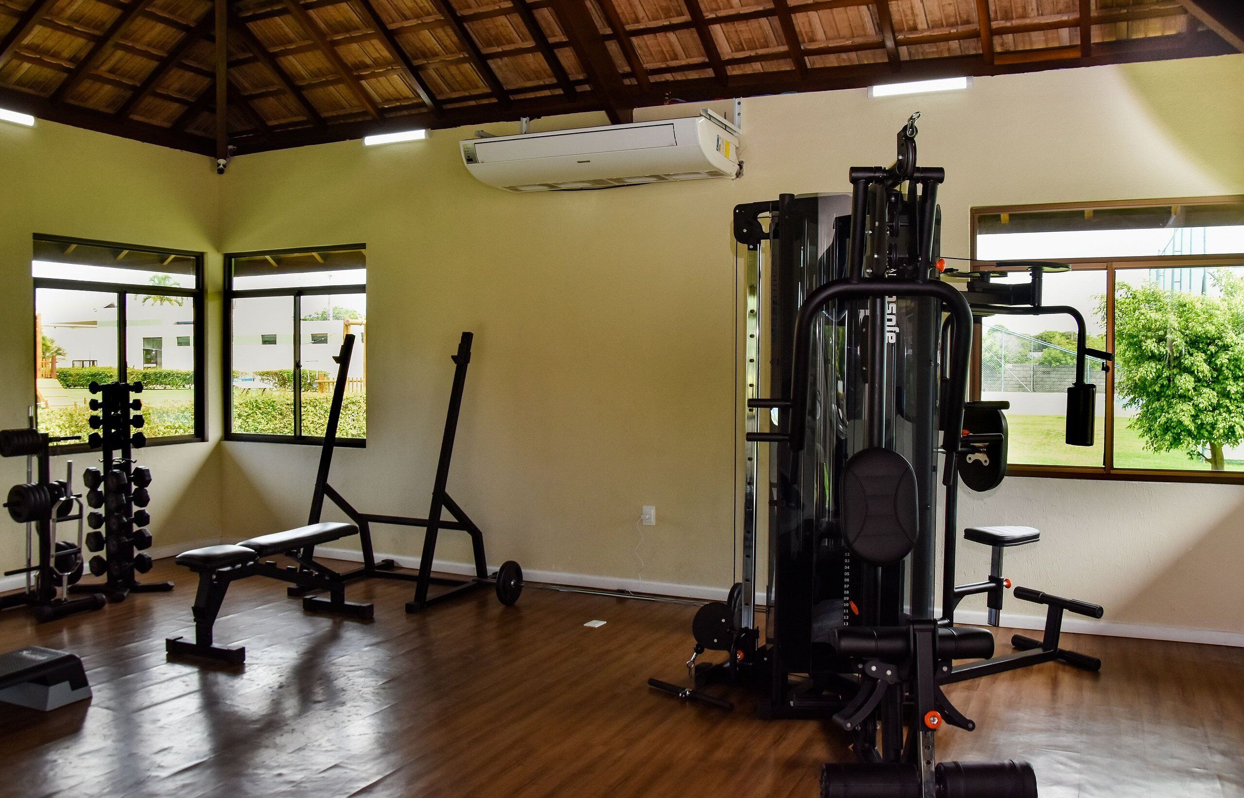 A gym with various exercise equipment, large windows, and a wooden floor.