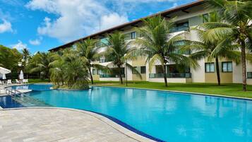 A swimming pool with a tiled edge, surrounded by palm trees and a building with multiple windows.