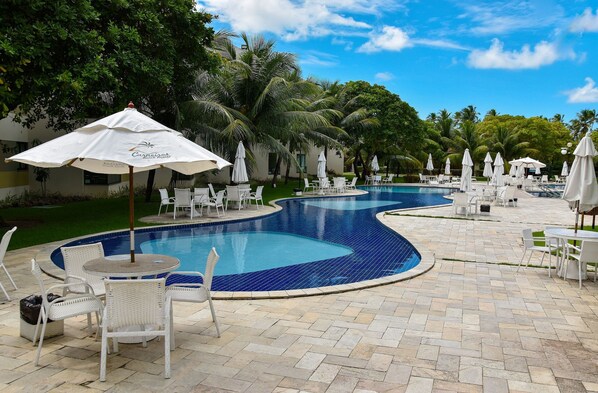 A pool area with white lounge chairs and umbrellas, surrounded by palm trees and a clear blue sky.