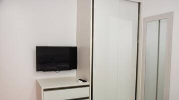 Un armario blanco con espejo, un televisor de pantalla plana montado encima y un pequeño escritorio blanco con un control remoto.