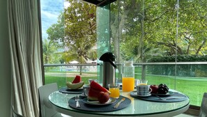 Una mesa de desayuno con cubierta de vidrio, una jarrón, una jarra de jugo de naranja y un cuenco de fruta.