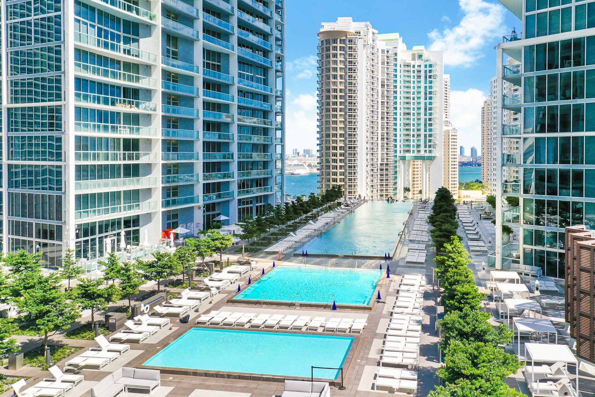 A high-rise hotel with multiple swimming pools, sun loungers, and a view of the city skyline.