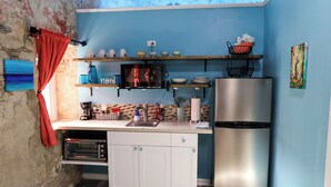 A compact kitchen with a microwave, toaster, and stainless steel refrigerator. There are shelves above the counter holding dishes and a basket with flowers. - Ground floor unit With local artist mural on exterior! (Frederiksted)