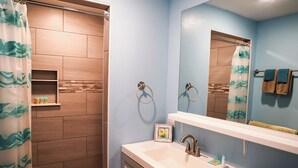 A bathroom with a shower, a sink, and a mirror. - Ground floor unit With local artist mural on exterior! (Frederiksted)