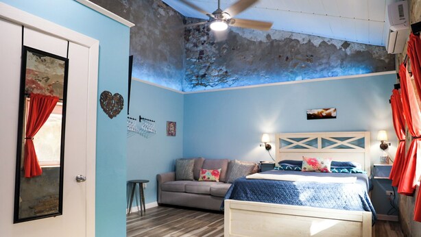 A bedroom with a bed, a sofa, and a ceiling fan. - Ground floor unit With local artist mural on exterior! (Frederiksted)