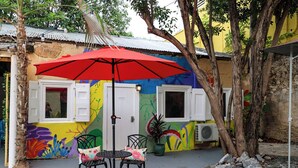 An outdoor seating area with a red umbrella, a table, and chairs. - Ground floor unit With local artist mural on exterior! (Frederiksted)