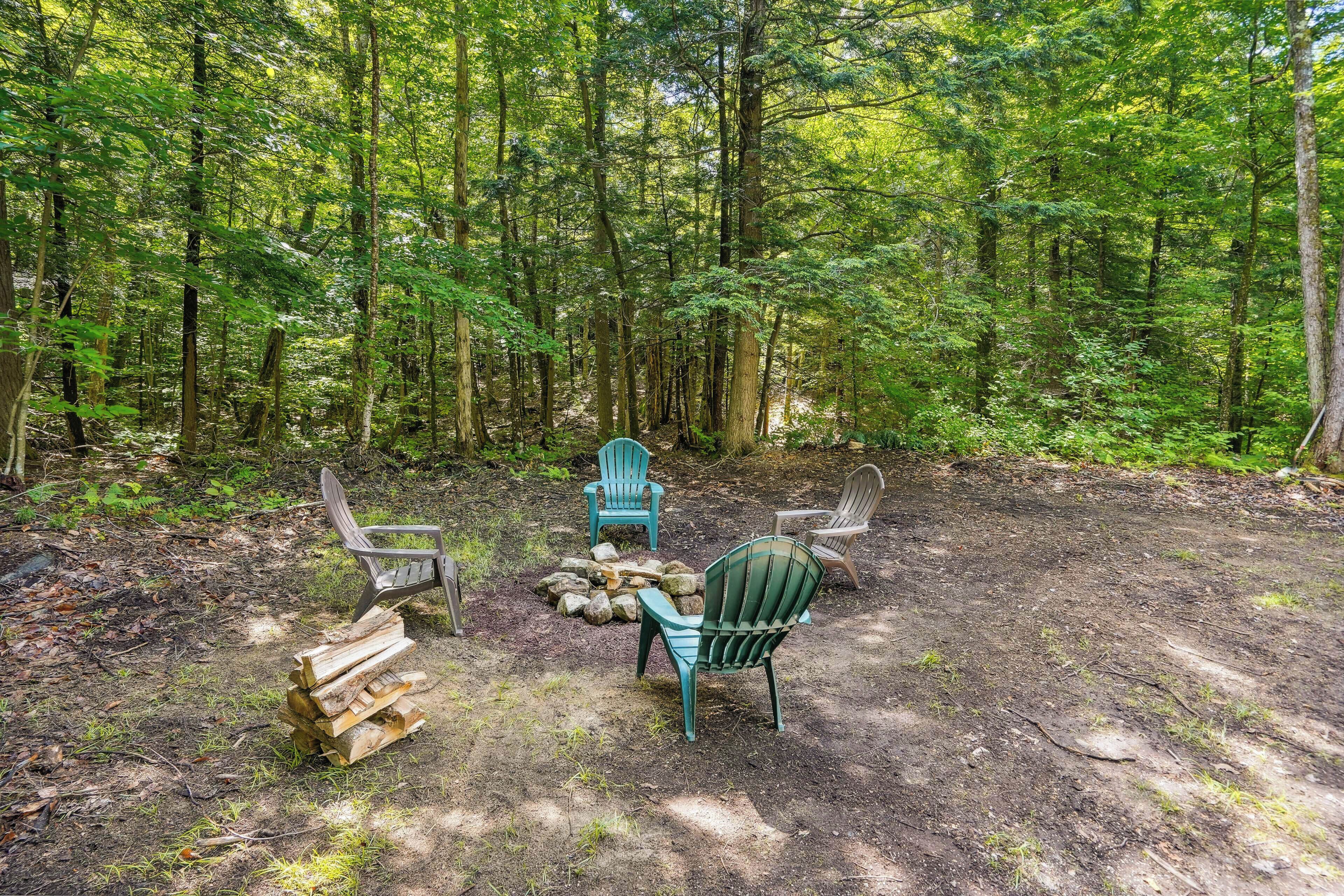 Une clairière dans la forêt, avec trois chaises Adirondack et une pile de bois de chauffage.