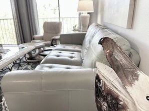 Een moderne woonkamer met een witte leren bank, een houten bijzettafeltje en een lamp.