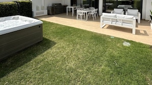 A modern multi-story building with a spacious outdoor patio area featuring a hot tub, outdoor seating, and a well-maintained lawn. - Luxurious Flat With Jacuzzi and Pool at Higueron (Fuengirola)