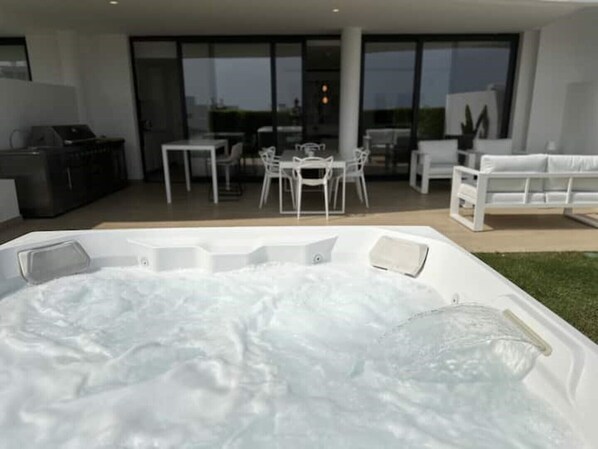 A modern outdoor hot tub area with a dining set and lounge chairs. - Luxurious Flat With Jacuzzi and Pool at Higueron (Fuengirola)