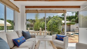 A modern living room with a beige sofa, a wooden coffee table, and a view of a garden and pool area through large sliding glass doors. - Casa del Limonero (Javea / Xàbia)