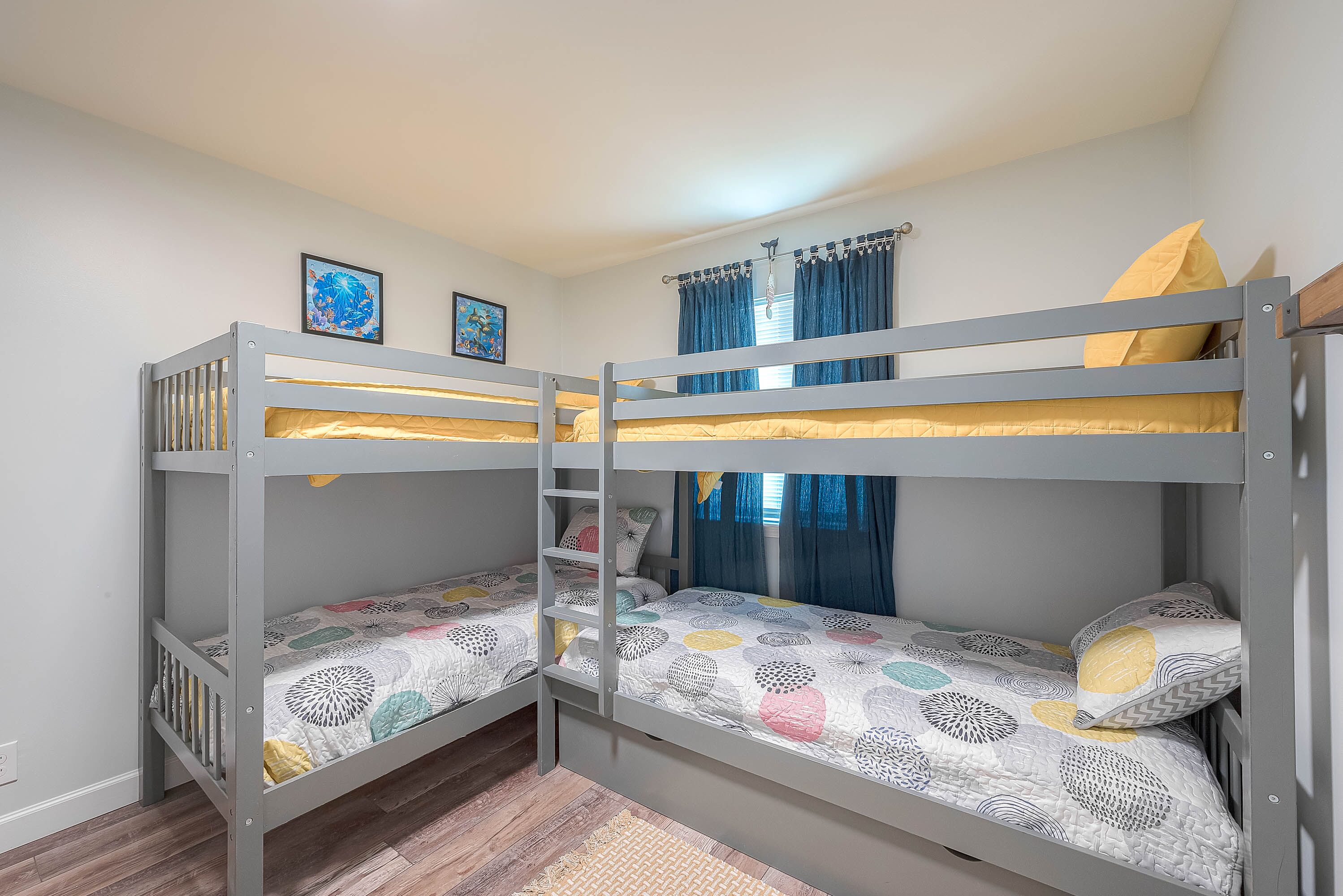 A bunk bed room with a ladder, two framed pictures on the wall, and a window with curtains.